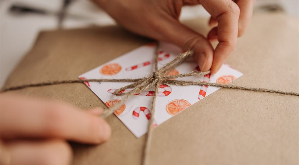 A gift tag being tied onto a parcel wrapped in brown paper