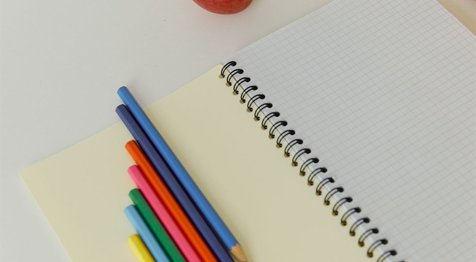 Coloured pencils and a spiral notebook on a desk